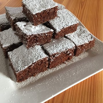 Schokokuchen mit Staubzucker bestreut und quadratisch geschnitten und auf einem Teller gestapelt angerichtet