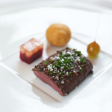 Hirschrücken mit Preiselbeerkrapferl und karamellisierter Haselnuss auf einem Teller edel angerichtet