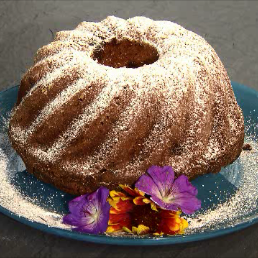 Guglhupf mit Staubzucker bestreut und auf einem Teller mit Blumen angerichtet
